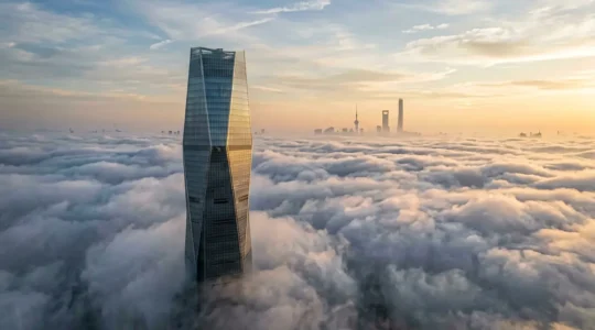 Vue aérienne d'une tour moderne émergeant des nuages avec Shanghai en arrière-plan